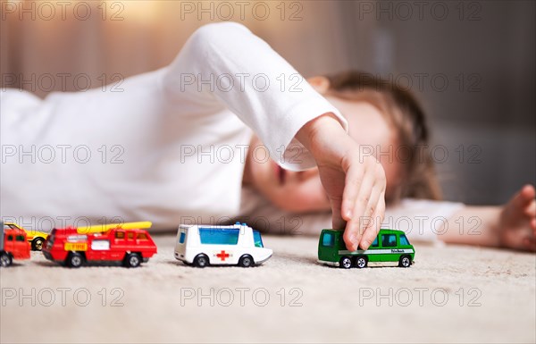 Young Girl Laying on Floor and Playing with Toy Cars and Trucks