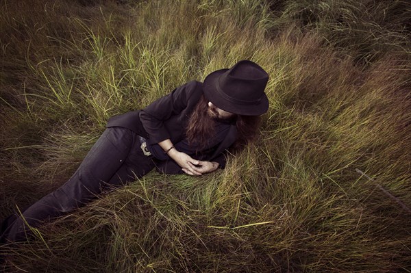 Young Adult Man in Hat and Suit Jacket Relaxing in Grass