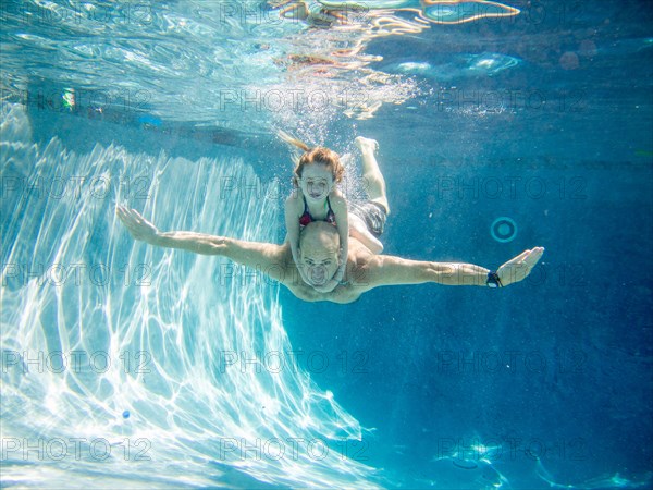 Father Swimming Underwater in Pool With Daughter on His Back