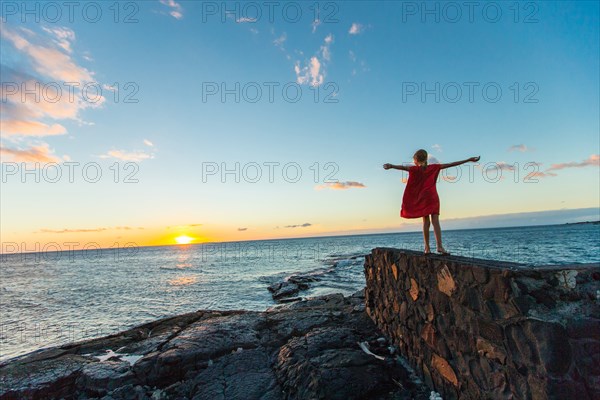 Rear View of Young Girl with Open Arms Greeting Sunrise on Ocean Beach, Kona Coast, Hawaii, USA