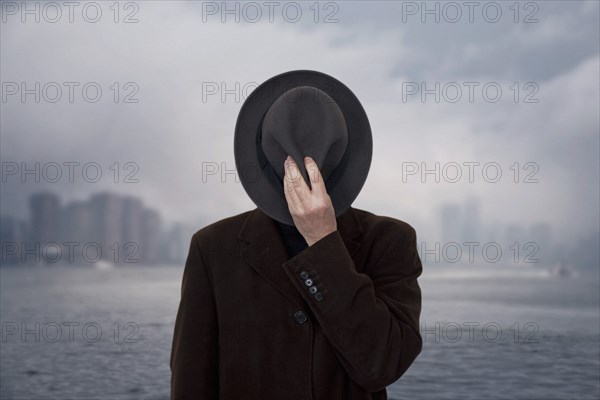 Man with Hat Covering his Face against Cloudy Sky