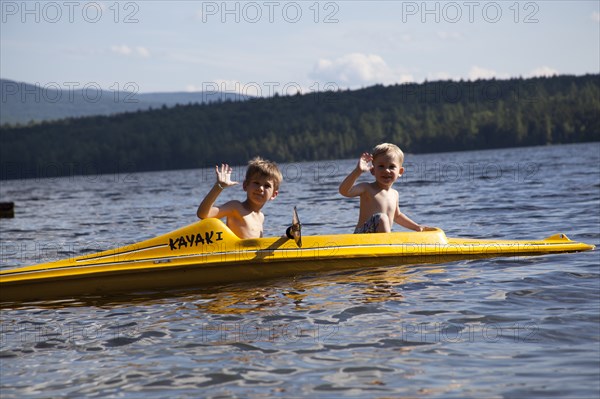 Two Young Boys Waving on Yellow Kayak on Lake