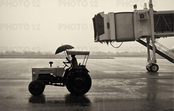 Man on Tractor Holding Umbrella at Airport