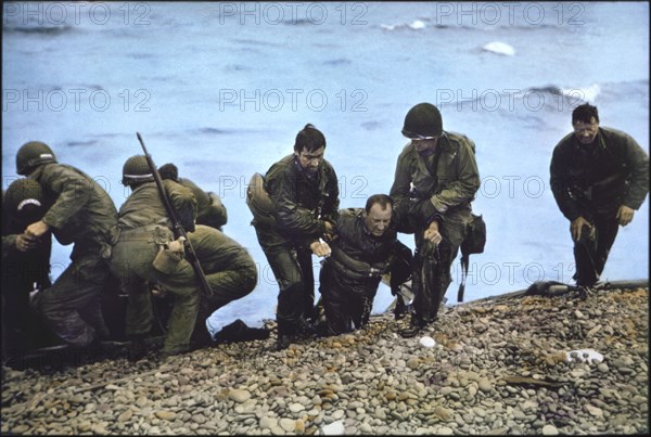 U.S. Soldiers of 116th Regiment of the 29th Infantry Division being helped to shore after Arriving at Omaha Beach in Life Raft after their Landing Craft Vehicle, Personnel (LCVP) had been Sunk off Beachhead, Nicholas Russin (3rd from right), being dragged onto shore by two Soldiers, Operation Overlord, Battle of Normandy, France, June 7, 1944