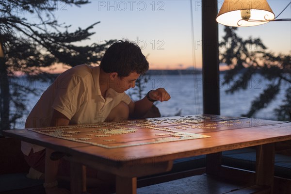 Teenage Boy Doing Jigsaw Puzzle at Lake House at Sunset