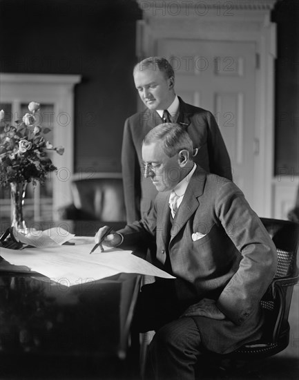 U.S. President Woodrow Wilson sitting at Desk in White House Oval Office with his Private Secretary Joseph Patrick Tumulty Standing nearby during Wilson's First Term in Office, Washington, D.C., USA, Harris & Ewing, between 1913 and 1916