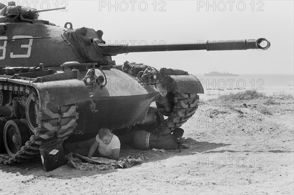 U.S. Soldier Reading Newspaper while another Solder rests in the shade under a U.S. Marine Tank in Beirut, Lebanon, Photograph by Thomas J. O'Halloran, July 1958