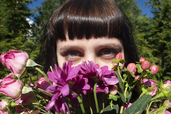 Portrait of Young Adult Woman Peering over Bouquet of Flowers