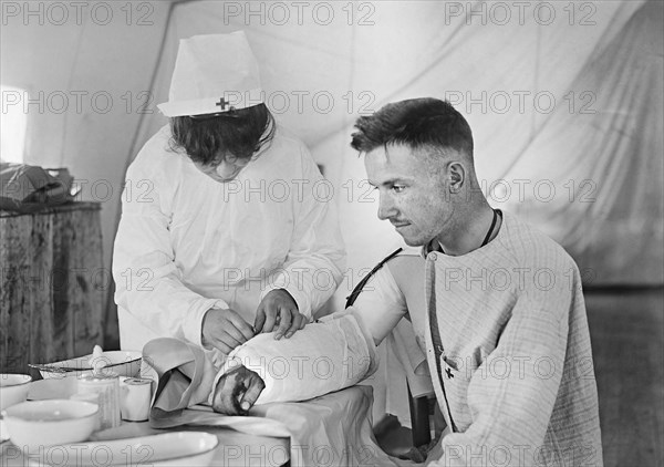 American Red Cross Nurse bandaging arm of Wounded American Soldier