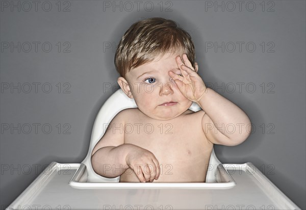 Tired Baby Boy rubbing his Eyes in High Chair