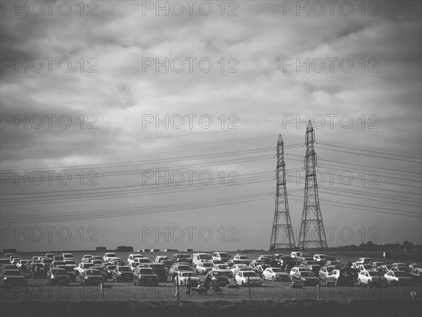 Multiple Cars Parked in Field with Electric Pylons in Background