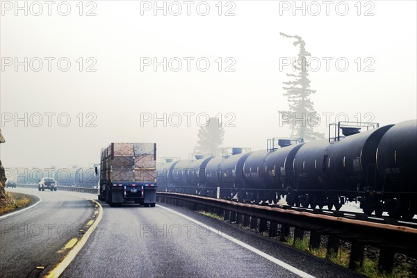 Wildfire smoke and highway traffic next to railway cars transporting oil,,