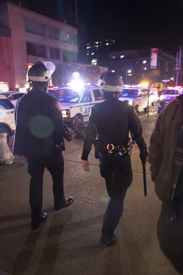 Rear View of Two Heavily Geared NYPD Officers walking with Helmets and Baton swinging, Lens Flare