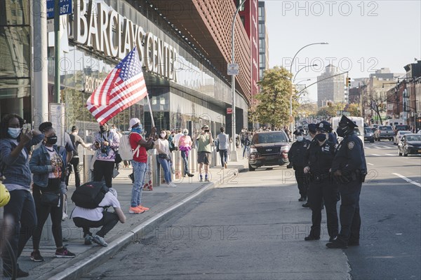 Man holding up American Flag at Barclays Center, opposite a Line of Police during Celebration of President-Elect Joe Biden
