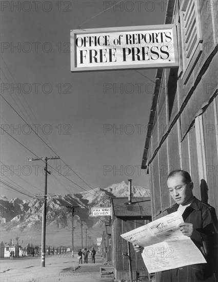 Editor Roy Takeno reading Copy of Manzanar Free Press in front of Newspaper Office