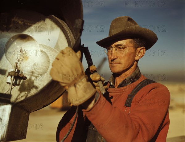 Man servicing floodlight at new construction of steel plant being built to aid war effort of steel production