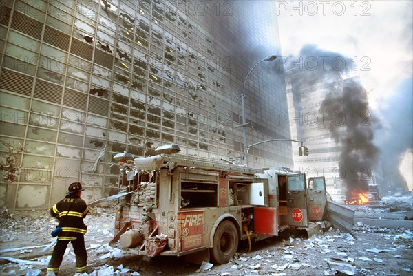 New York City fire fighter pulling water hose from fire truck amid debris and burning buildings following September 11th terrorist attack on World Trade Center