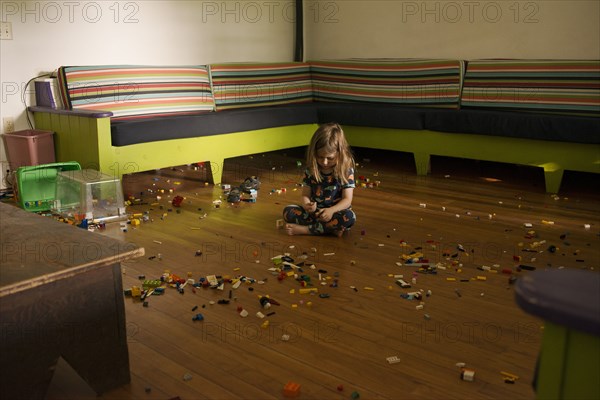 Young Boy sitting on Floor of Large Room surrounded by Plastic Toy Pieces