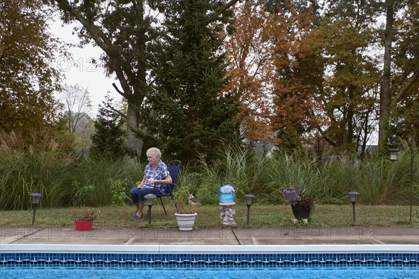 Contemplative Elderly Woman sitting in Chair near Swimming Pool