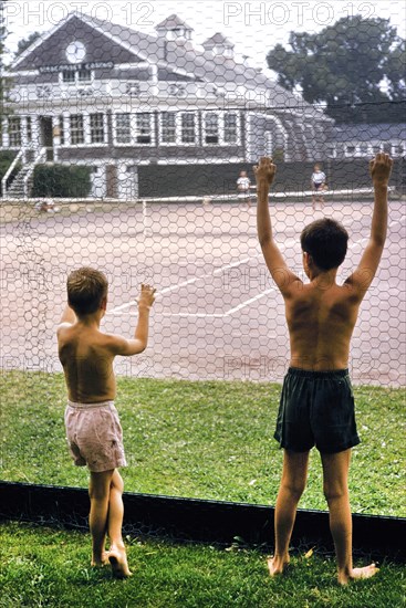 Rear View of Two Shirtless Young Boys watching Tennis Match through Fence