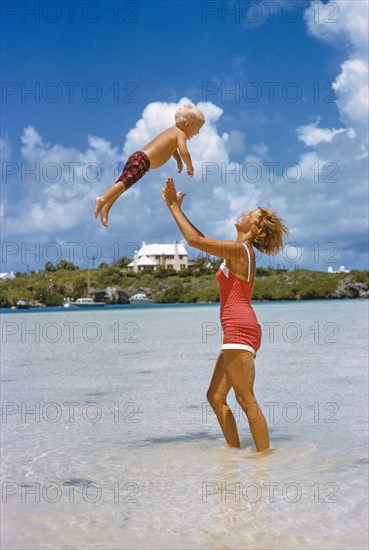 Woman playfully tossing Young Boy in Air at Beach