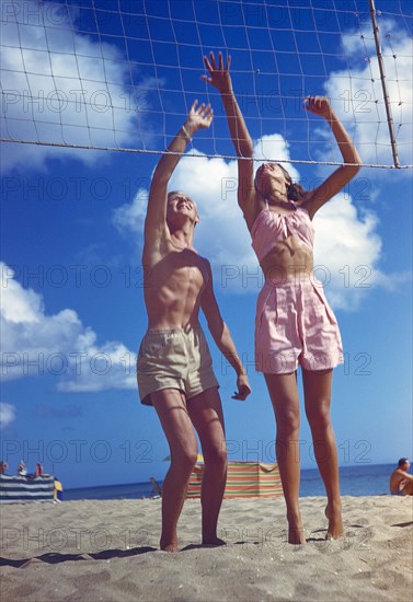 Young Adult Man and Young Adult Woman playing Volleyball on Beach
