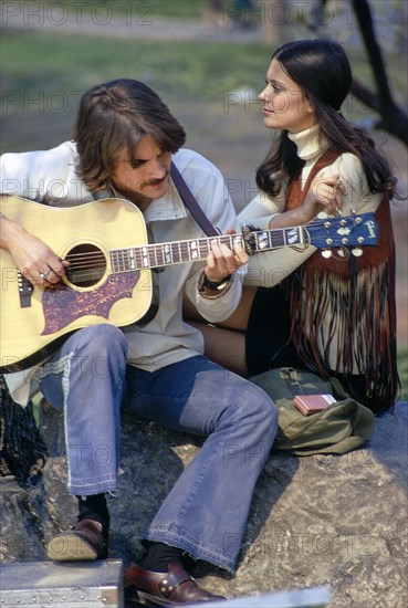 Young Adult Woman listening to Young Adult Man playing Acoustic Guitar