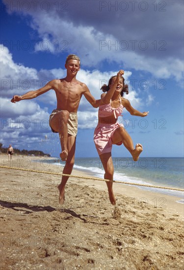 Young Adult Man and Young Adult Woman jumping over Rope on Sandy Beach