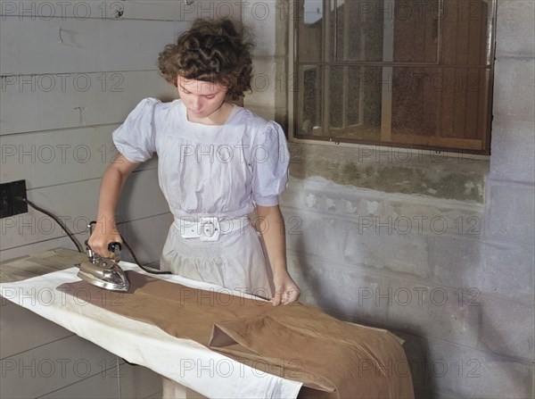 Young Adult Woman ironing Trousers at Laundry Facilities in Utility Building