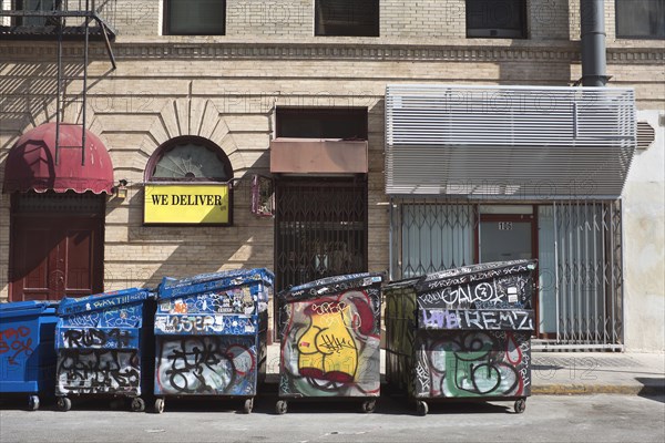 Five Garbage Dumpsters covered in Graffiti along Curb