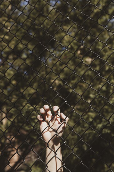 Hand holding black chain link fence at Anti-Asian Violence Rally