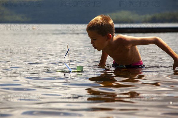 Young boy with homemade toy sailboat in lake