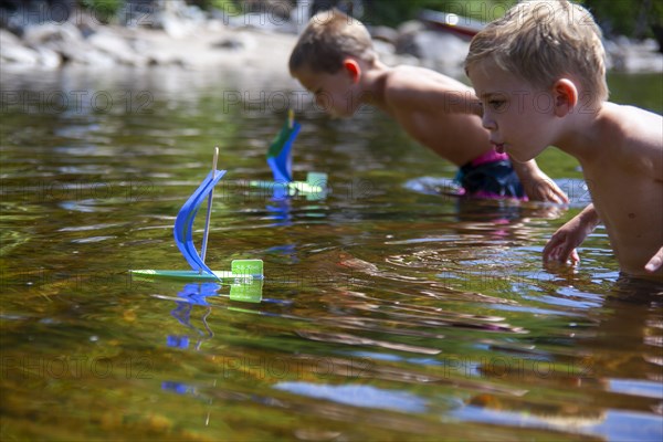 Two young boys with homemade toy sailboats in lake