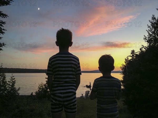 Rear view of two young boys viewing sunset at lake