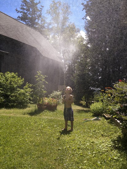 Young boy playing with sprinkler hose in yard