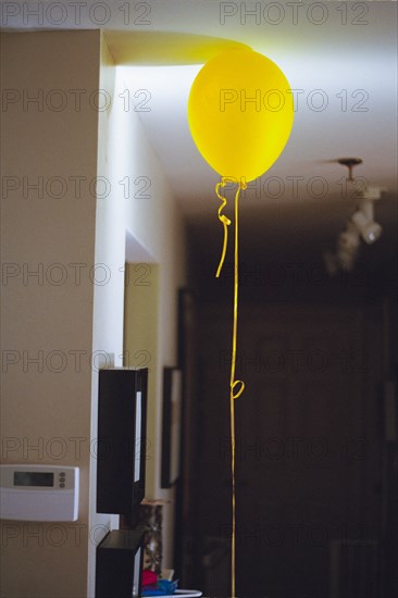 Yellow helium balloon with long string on apartment ceiling