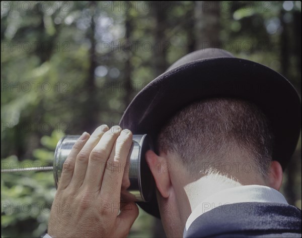 Rear view of man with ear to tin cup telephone