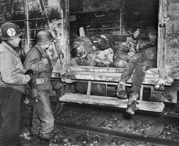 Two U.S. soldiers looking at dead prisoners on railroad train at unidentified concentration camp