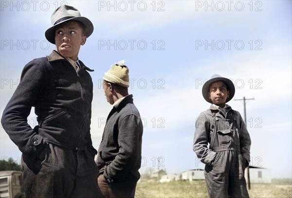 Three teen boys watching construction of prefabricated houses built by U.S. Farm Security Administration for farmers being relocated due to construction of Camp Croft