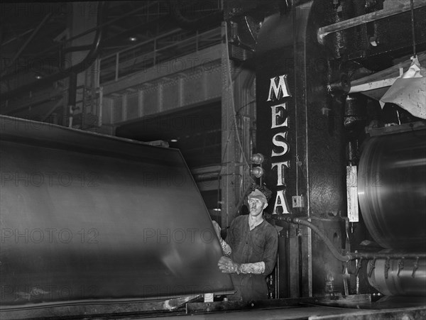 Steel worker examining sheet of steel after rolling