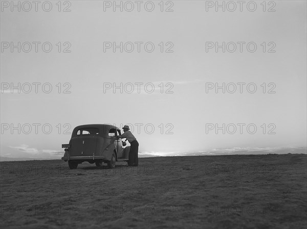 Man standing at car window talking to driver on the plain at sunset