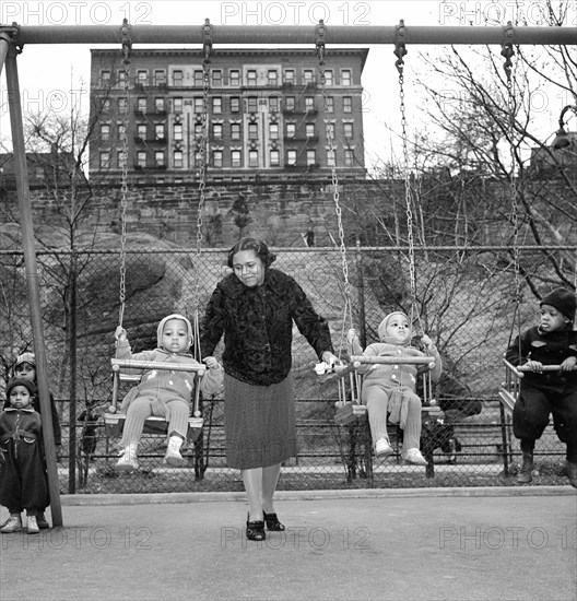 Woman pushing young children on swings at urban playground