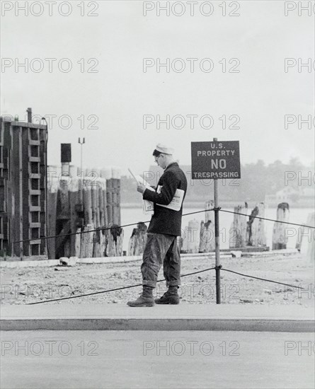 Man reading a newspaper next to sign reading  "U.S. property