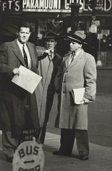 Three businessmen in overcoats talking on sidewalk