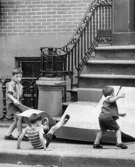 Three young boys  using cardboard to slide down front steps of apartment building