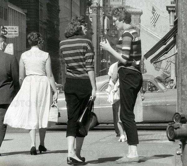 Two women in striped sweaters chatting on a sidewalk corner