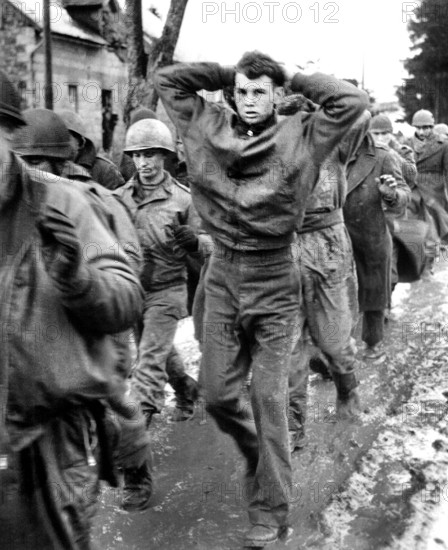 U.S. soldier with hands clasped behind his head, leading a file of American prisoners captured by Germans during surprise enemy drive into Allied positions on Western Front, German film captured by the U.S. Army Signal Corps, December 1944
