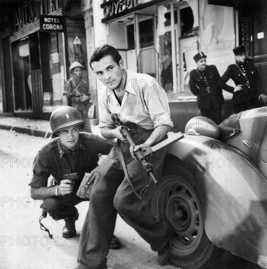 American officer and French partisan crouch behind an auto during a street fight, France, U.S. Army Signal Corps, 1944