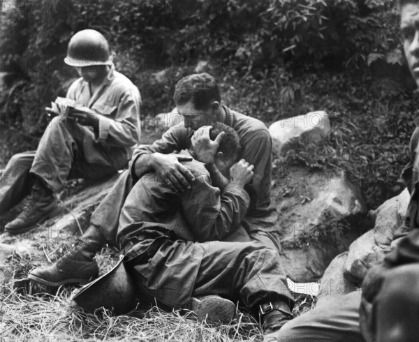 Grief stricken American infantryman whose buddy had been killed in action being comforted by another soldier. In the background a corpsman methodically fills out casualty tags, Haktong-ni area, Korea, U.S. Army Signal Corps, August 28, 1950