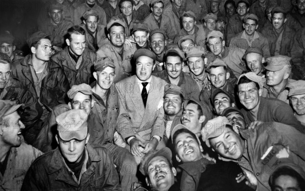 Bob Hope, radio and screen star, sitting with men of X Corps, as members of his troupe entertain, Wonsan, Korea, U.S. Army Signal Corps, October 26, 1950